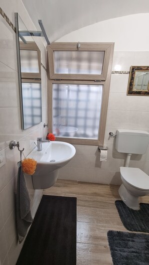 A bathroom with a white sink, a toilet, a window with a wooden frame, and a mirror. - Beautifully restored romantic apartment in the centre of historic Dolcedo (Dolcedo)