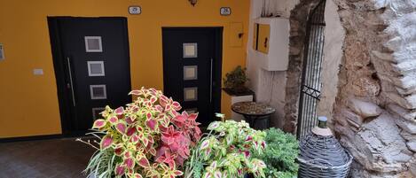A hotel entrance with two black doors, a yellow wall, and a stone wall with a gate.