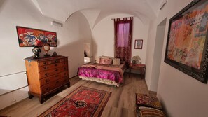 A bedroom with a wooden dresser, a bed with a pink bedspread, a red rug, and a painting on the wall. - Beautifully restored romantic apartment in the centre of historic Dolcedo (Dolcedo)