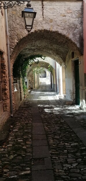 A cobblestone alleyway with stone arches, a hanging lantern, and a narrow path flanked by buildings. - Beautifully restored romantic apartment in the centre of historic Dolcedo (Dolcedo)