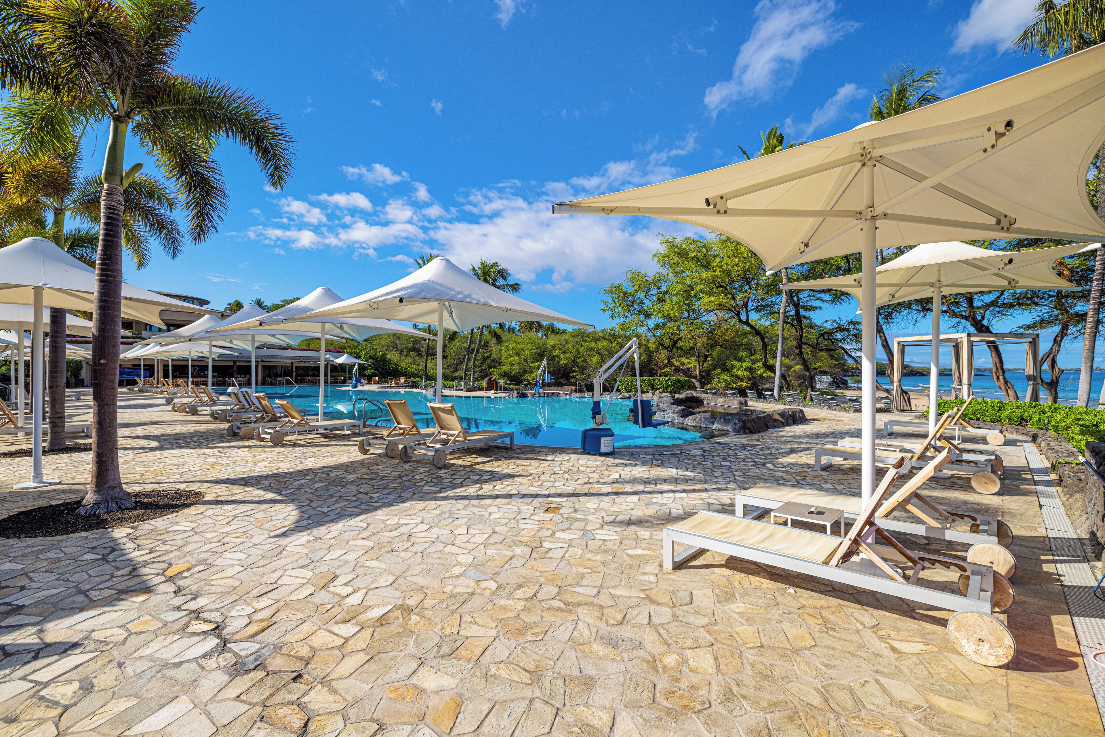 A poolside area with lounge chairs, umbrellas, and a stone-tiled floor.