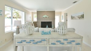 Uma sala de estar com lareira, uma mesa com gavetas em formato de peixe e uma placa com a inscrição 'Beach'.