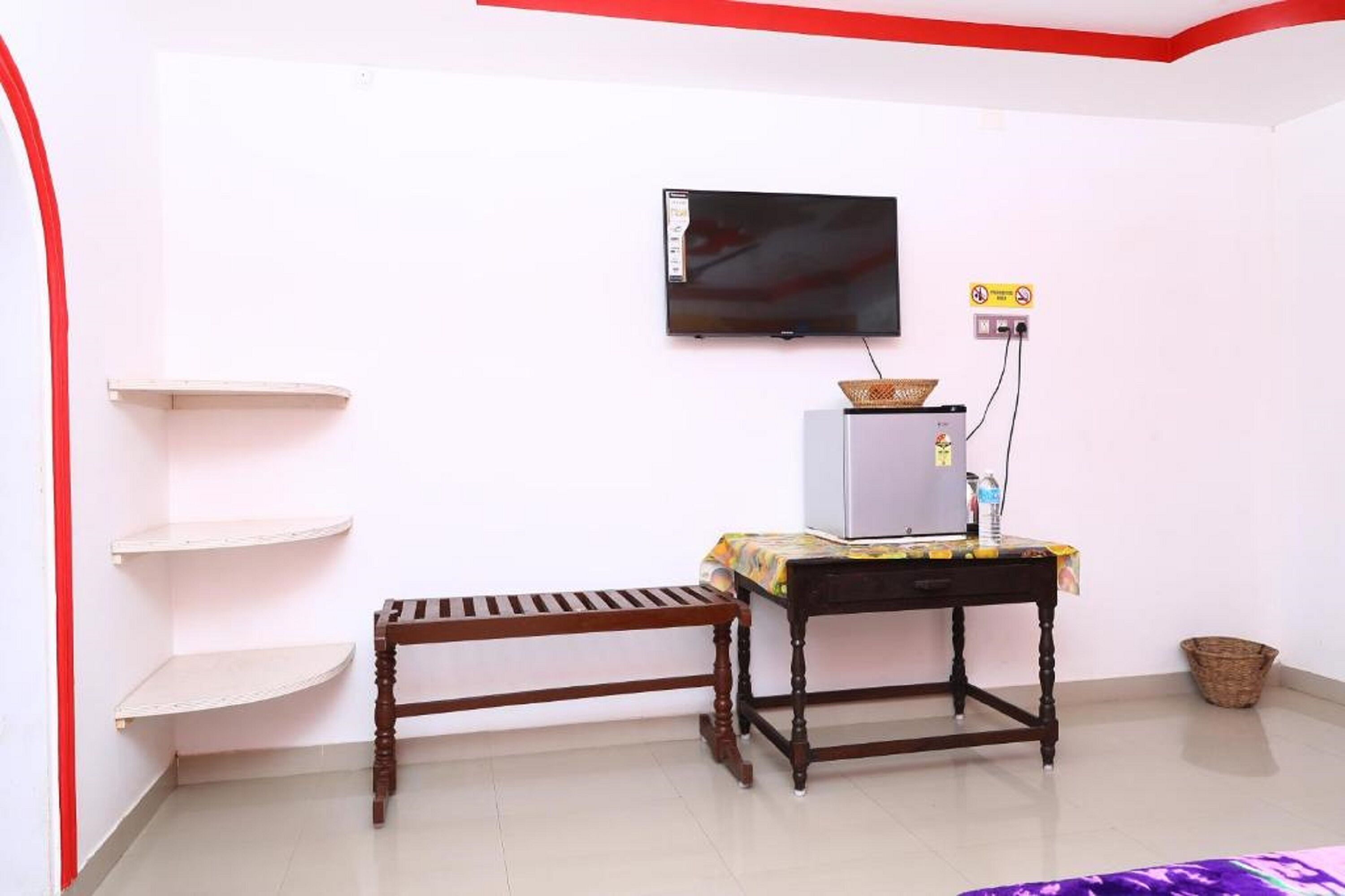 A room with a television mounted on the wall, a small table with a basket, and a bench.