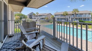 A balcony with wooden chairs and a view of a swimming pool and apartment buildings. - Second row, three bed, two bath condo, complex pool (Surfside Beach)