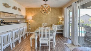 A kitchen with a wooden wall, a dining area with white chairs, a chandelier, and a view of the outside. - Second row, three bed, two bath condo, complex pool (Surfside Beach)