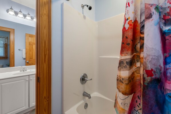 A bathroom with a white bathtub, a wooden door, and a mirror.