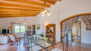 A spacious dining area with a glass table surrounded by metal chairs, wooden ceiling beams, and a chandelier. - Rural finca in Mallorca Els Moyans with pool (Muro)