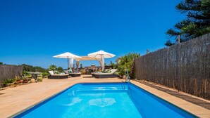 A swimming pool with lounge chairs and umbrellas, surrounded by a wooden fence and greenery. - Rural finca in Mallorca Els Moyans with pool (Muro)