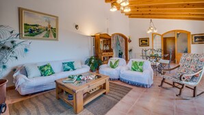 A living room with a wooden ceiling, a white sofa set, a coffee table, and a dining area with a table and chairs. - Rural finca in Mallorca Els Moyans with pool (Muro)