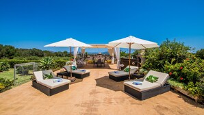 An outdoor patio with four lounge chairs and two umbrellas, surrounded by lush greenery and a clear blue sky. - Rural finca in Mallorca Els Moyans with pool (Muro)
