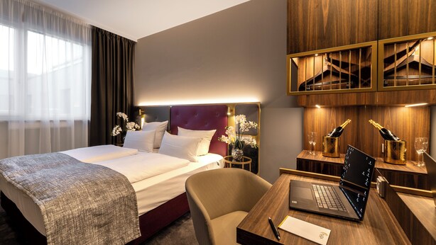 A hotel room with a large bed, a desk with a laptop, and a minibar.