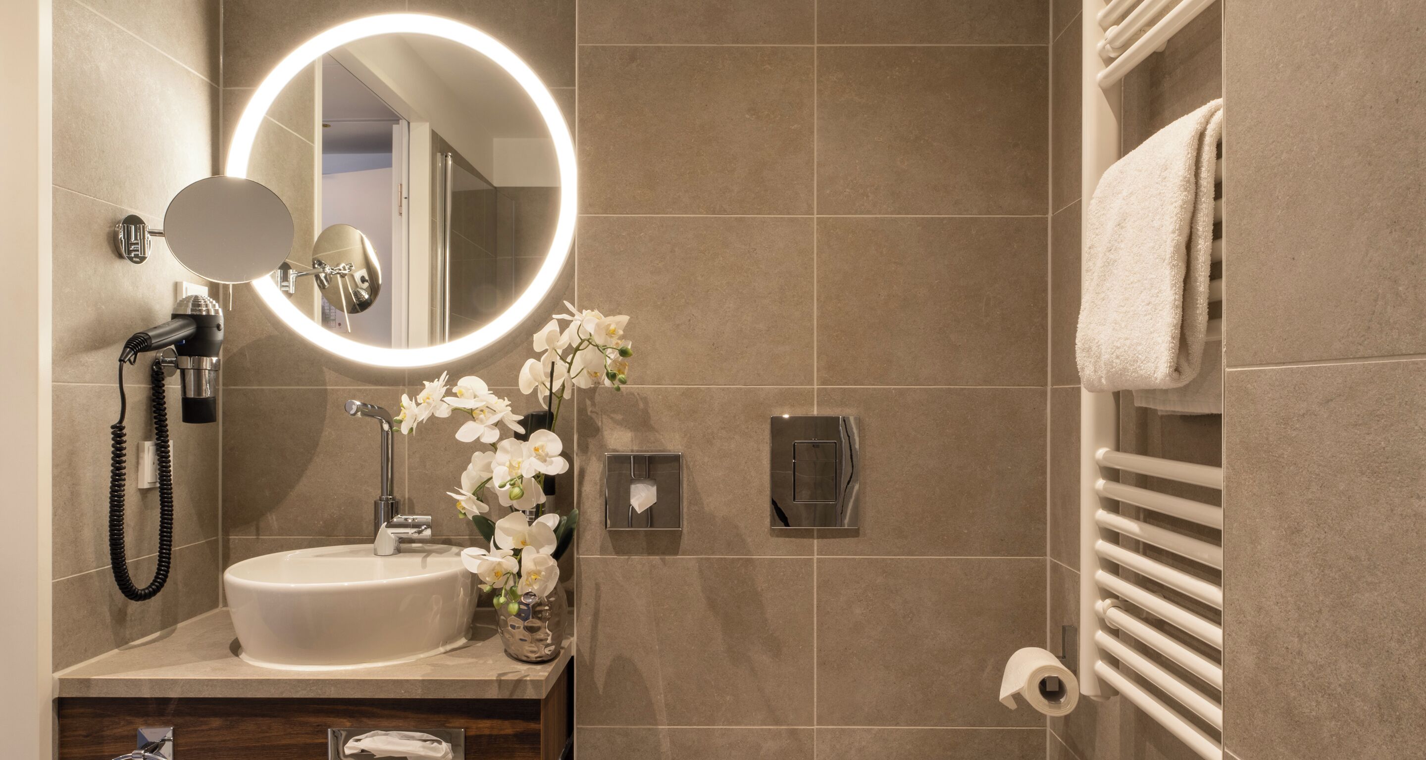 A modern bathroom with a round mirror, a sink, a hairdryer, and a towel rack.