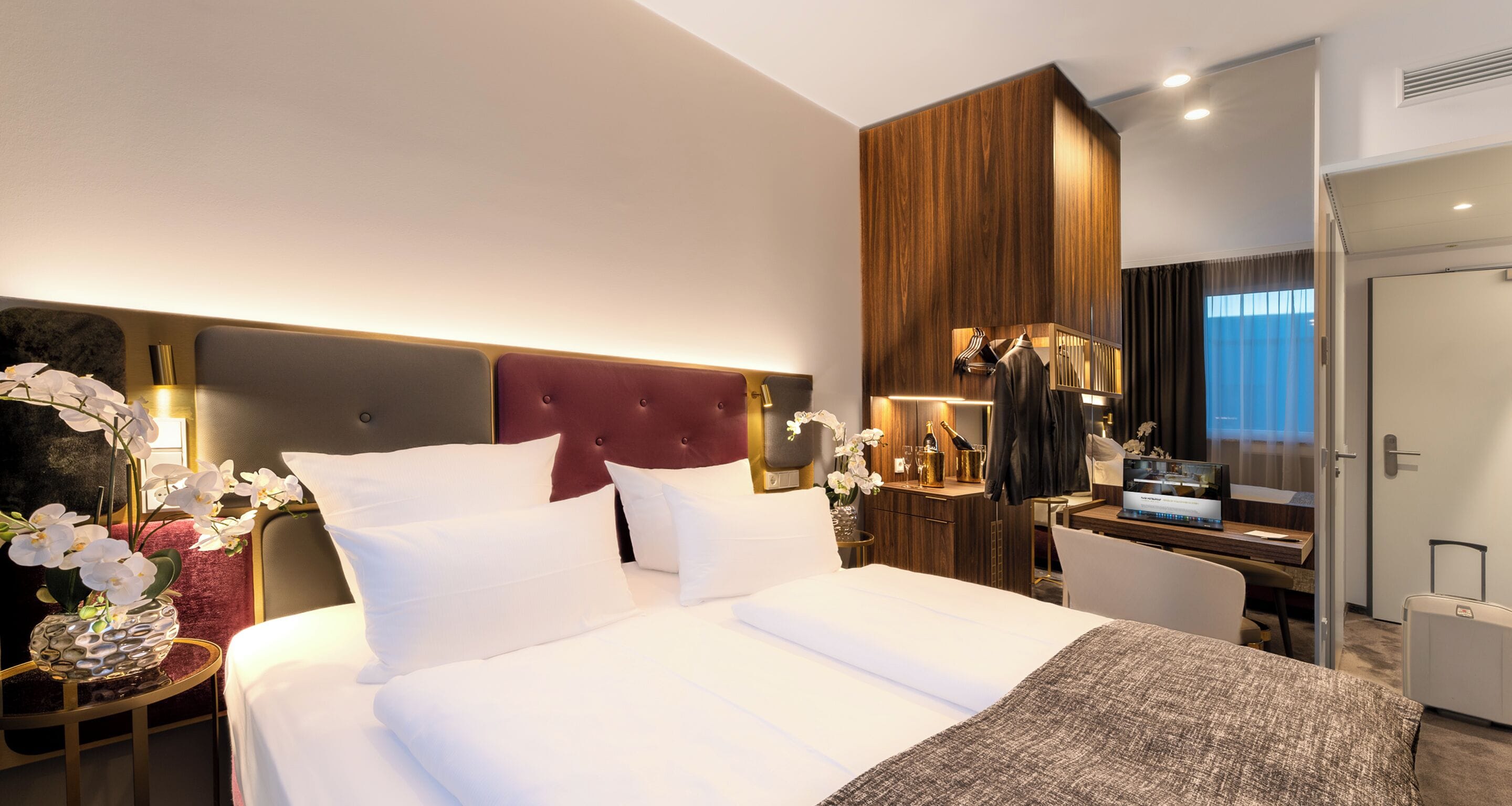 A hotel room with a large bed, a desk, and a wardrobe.