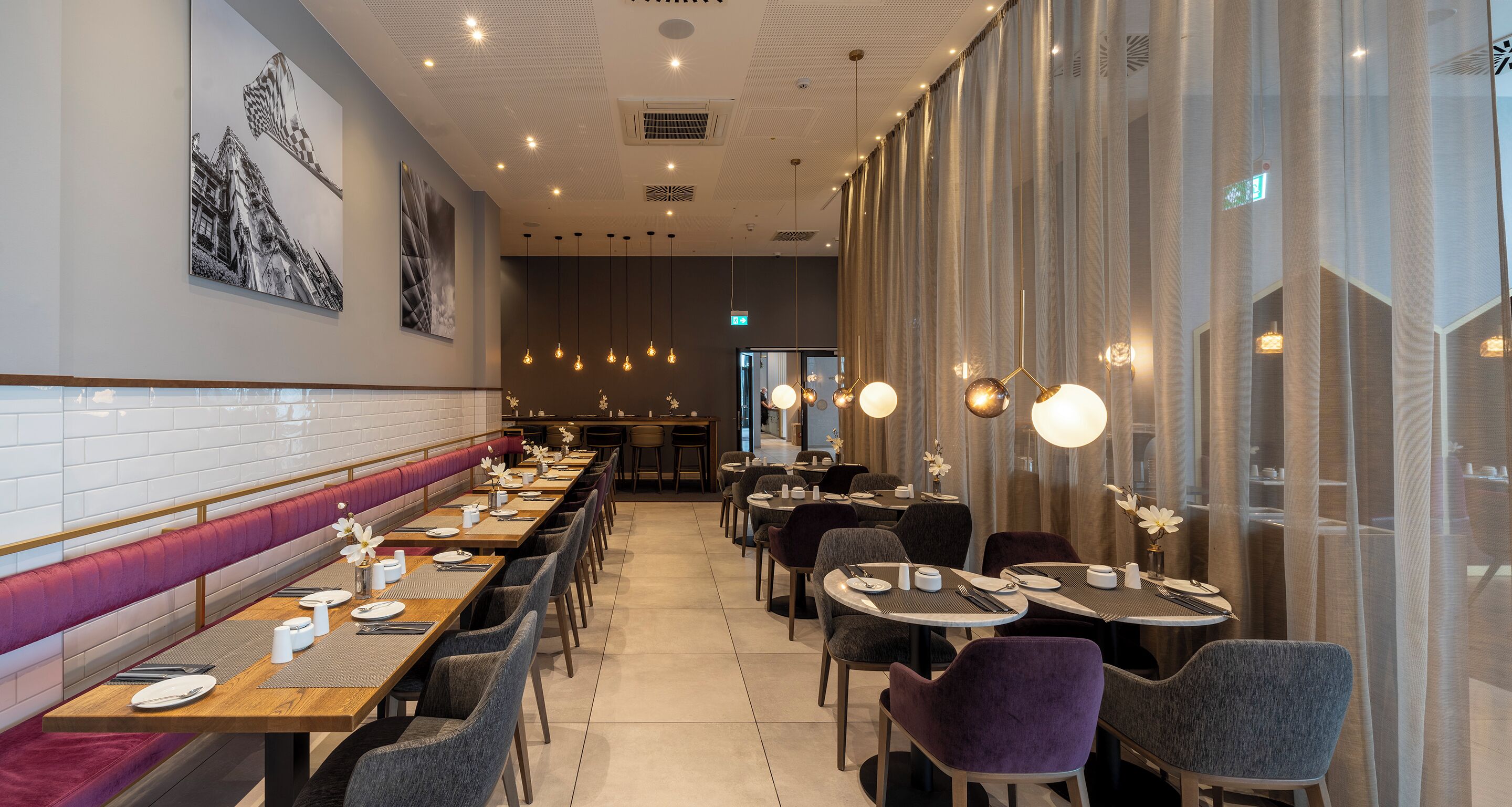 A restaurant with long communal tables, individual booths, and hanging pendant lights.