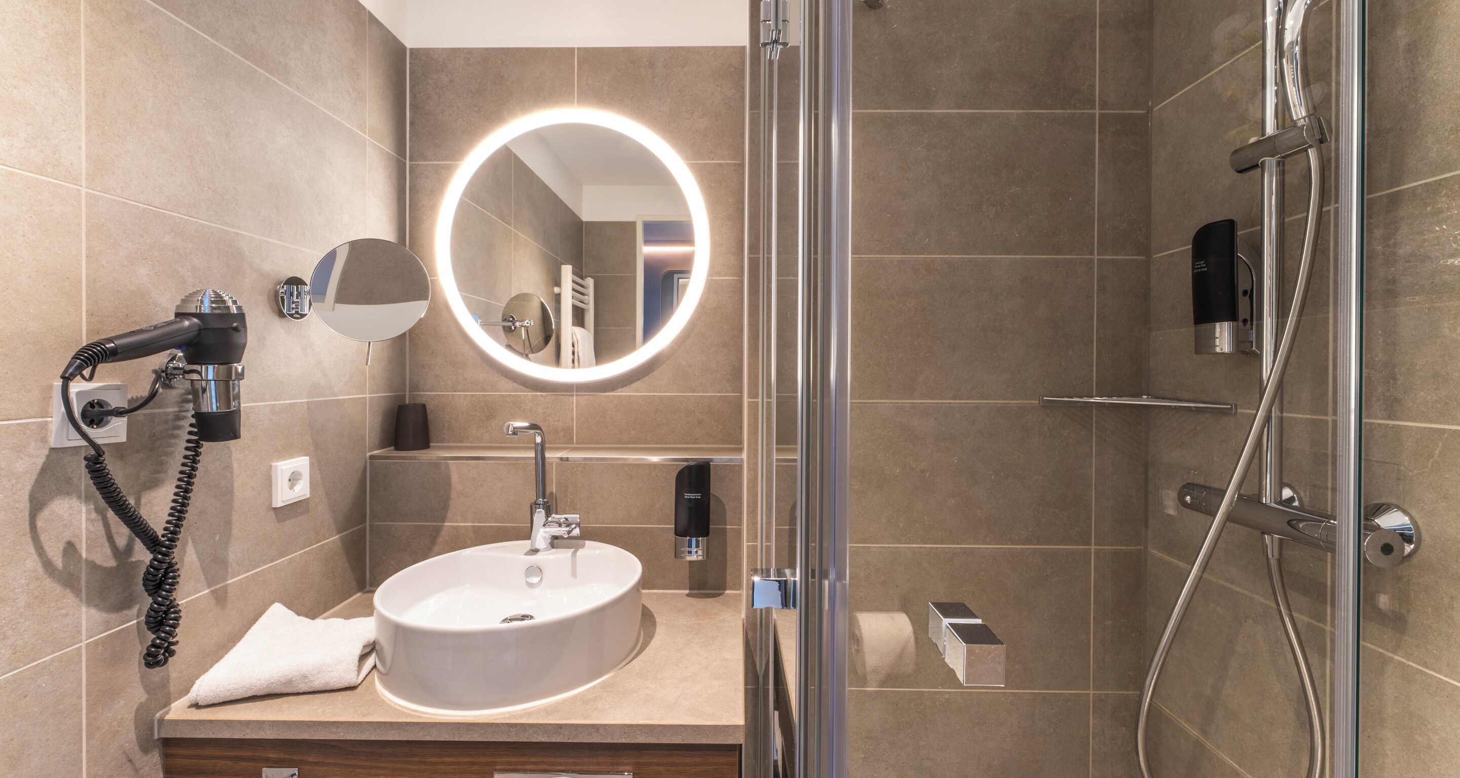 A modern bathroom with a round mirror, a sink, a handheld showerhead, and a glass-enclosed shower.