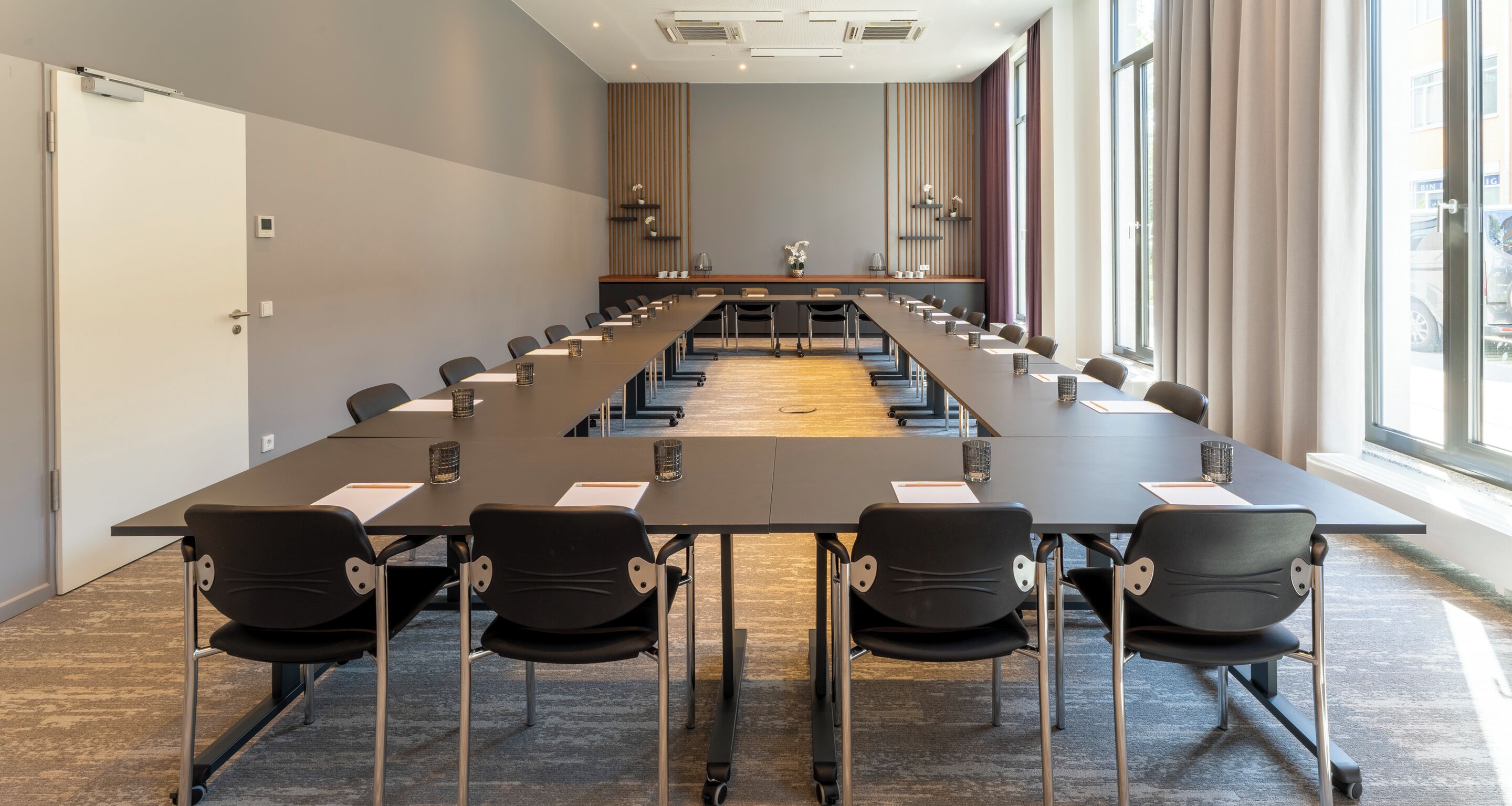 Une salle de conférence avec une longue table, des chaises et une vue sur l’extérieur grâce à de grandes fenêtres.