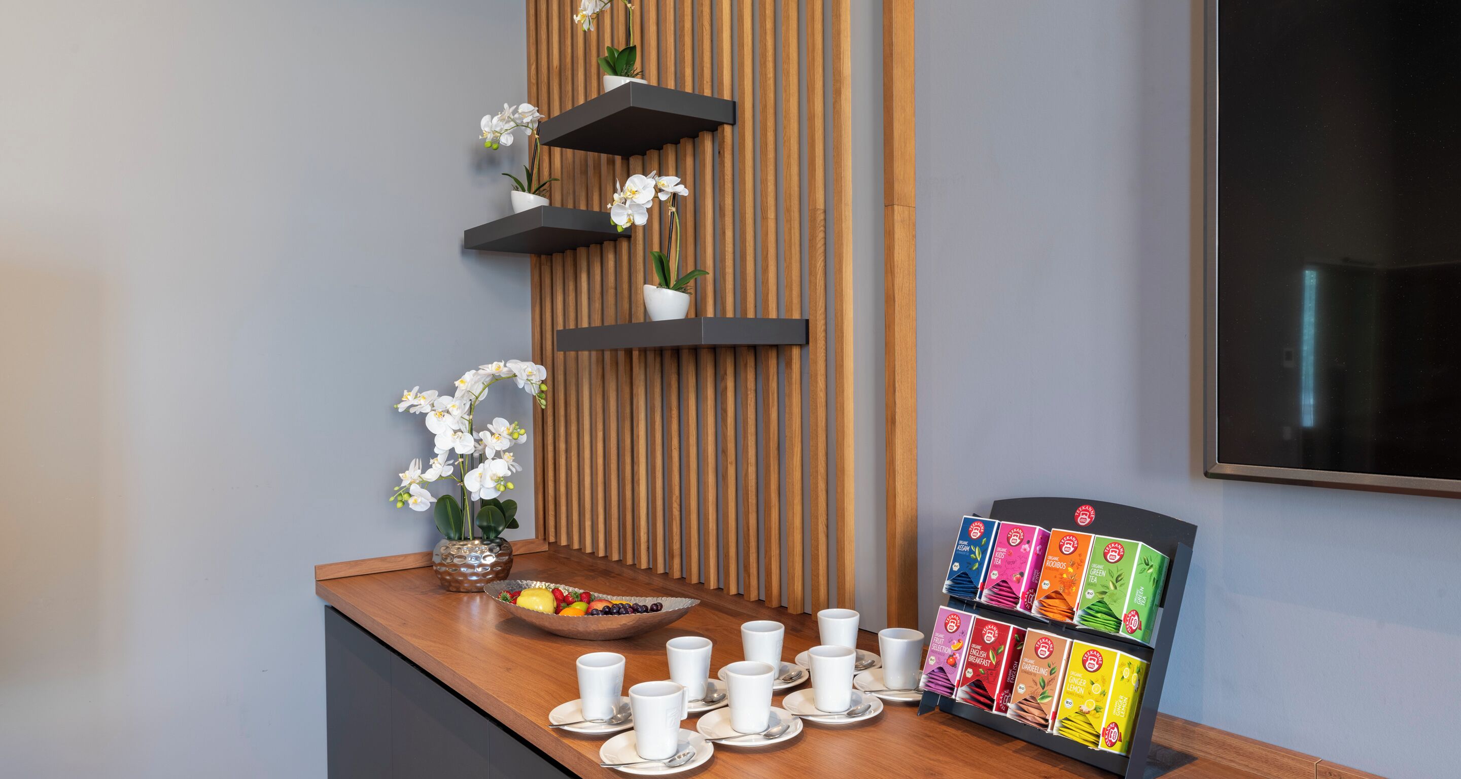 A reception area with a wooden panel wall, a fruit bowl, white cups, saucers, and a colorful display stand.