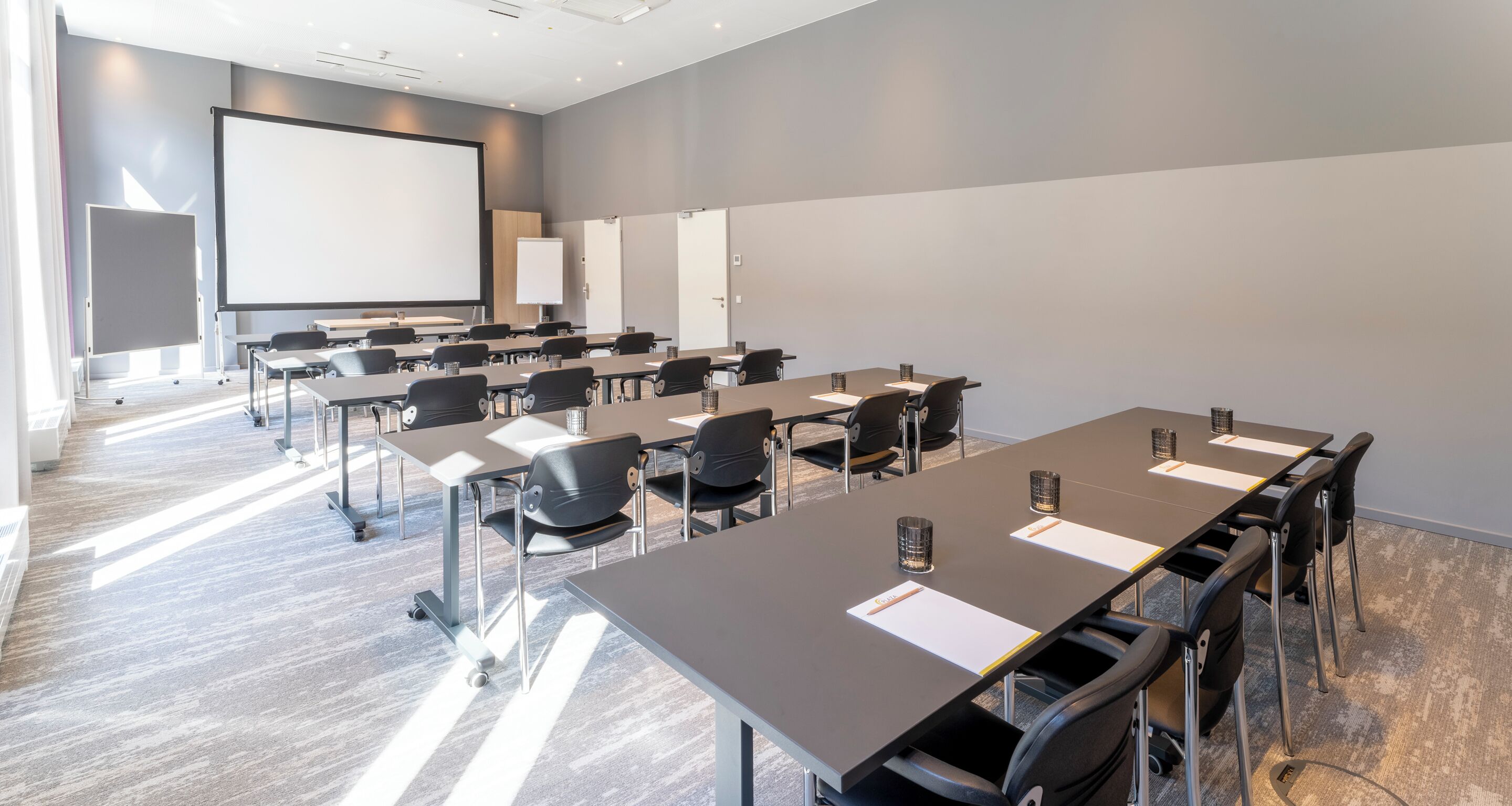 Un salón de conferencias con una pantalla grande, varias mesas y sillas.