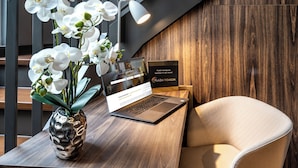 A laptop on a desk with a vase of orchids, a sign for Plaza Hotelgroup, and a wooden wall. - PLAZA Premium München (Munich)