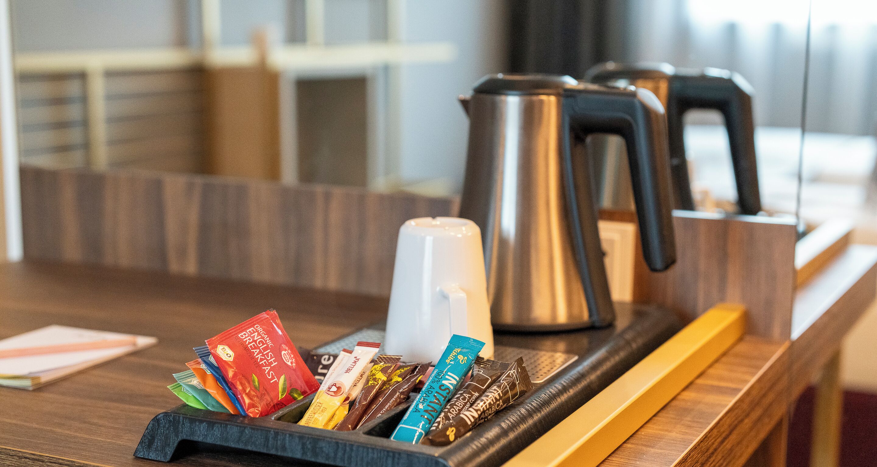 Una barra de desayuno equipada con cafetera, hervidor y una bandeja con distintos productos para el desayuno.