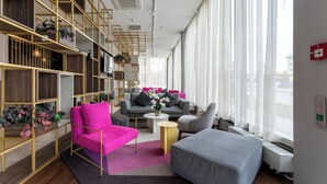 A modern living room with a sofa, armchair, and ottoman, a bookshelf, and a large window with curtains. - PLAZA Premium München (Munich)