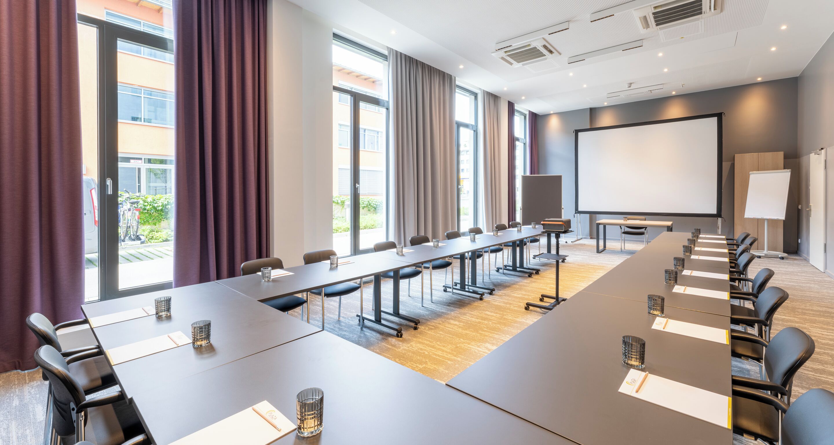 Un salón de conferencias con una mesa grande, sillas, una pantalla de proyector y una pizarra.