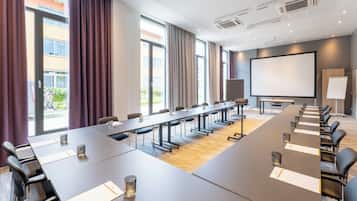 Un salón de conferencias con una mesa grande, sillas, una pantalla de proyector y una pizarra.