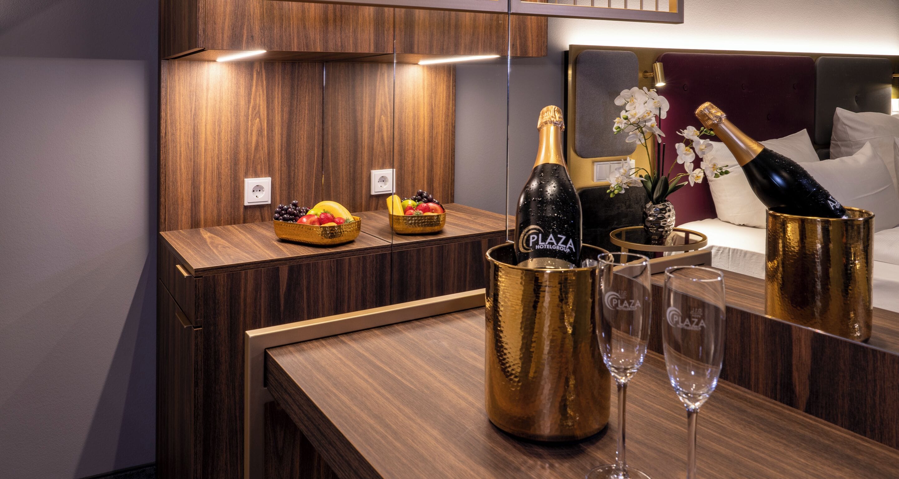 A wooden table with a fruit bowl, a bottle of champagne, and two glasses.