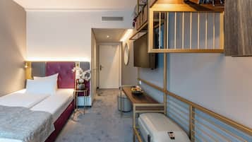 Una habitación de hotel con cama, mesita de noche, lámpara y un escritorio pequeño con una silla.