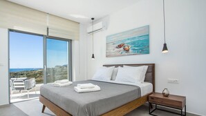Ein modernes Schlafzimmer mit einem großen Bett, einem Gemälde von Booten und Blick aufs Meer.