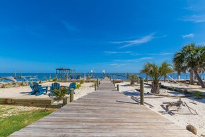 Une promenade en bois menant à une plage où l’on trouve des chaises bleues et des palmiers.