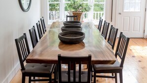 A dining room with a large wooden table surrounded by chairs, large windows, and a view of greenery outside. - Historical Bed and breakfast<br> (Water Mill)