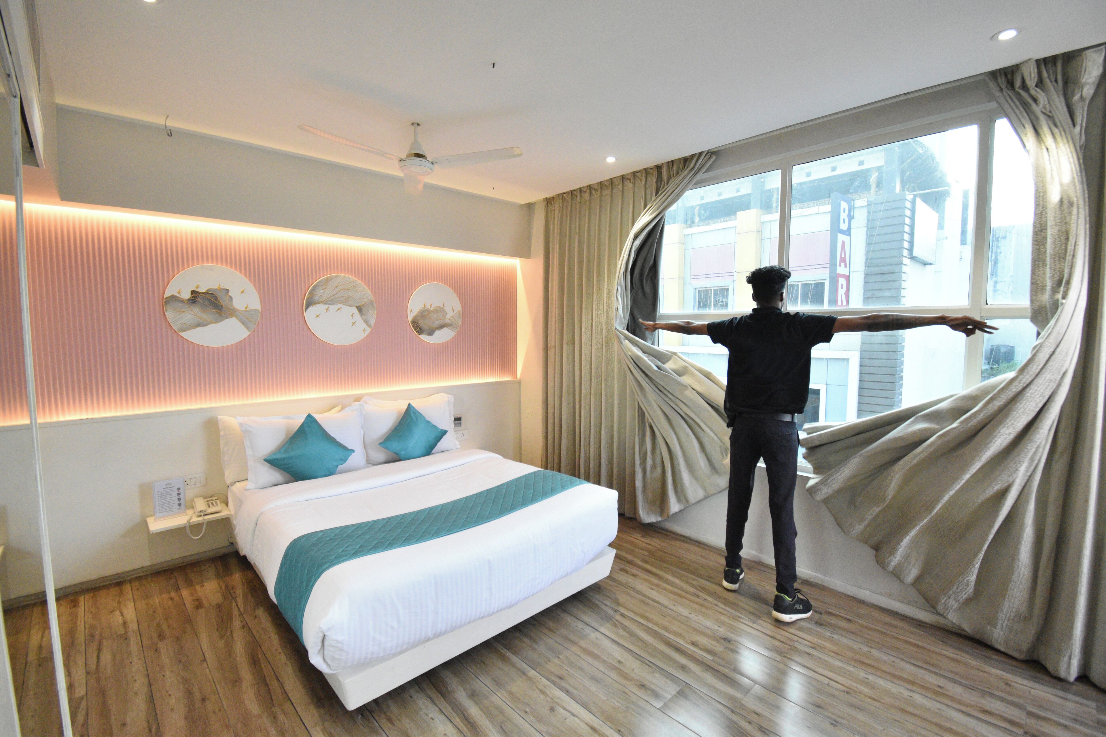 A hotel room with a bed, a ceiling fan, a window with curtains, and a wall with circular mirrors.