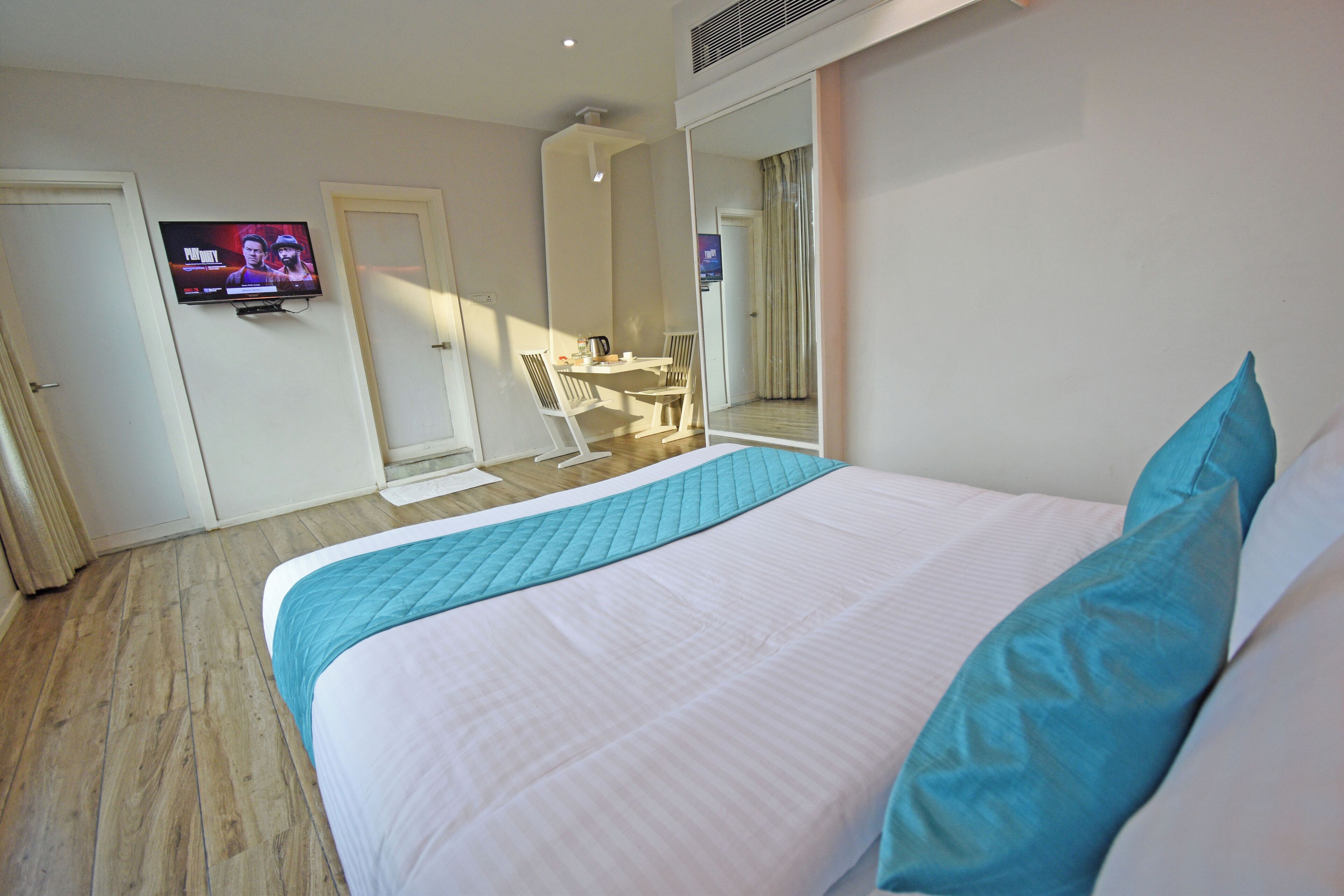 Une chambre d’hôtel avec un grand lit, un tél éviseur fixé au mur et un miroir qui reflète la pièce.