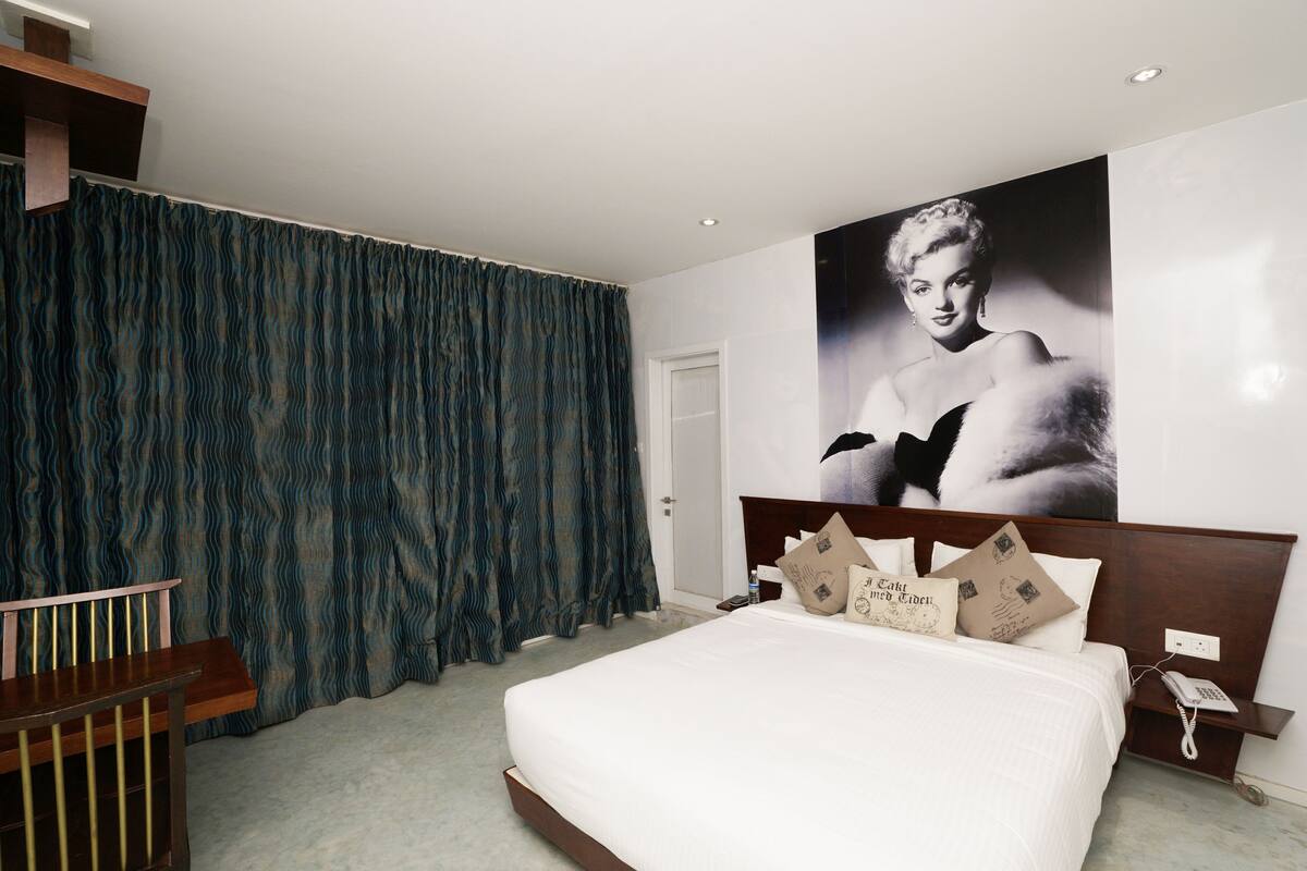 Un dormitorio con una cama grande, cabecera de madera, mesita de noche, teléfono y un cuadro colgado en la pared.