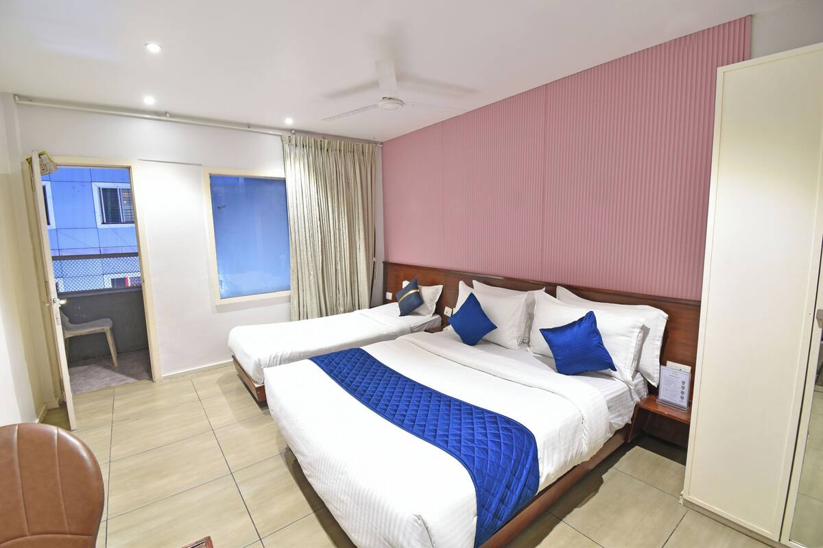 Habitación de hotel con dos camas, cabecero de madera, ventilador de techo, ventana con cortinas y un pequeño escritorio.