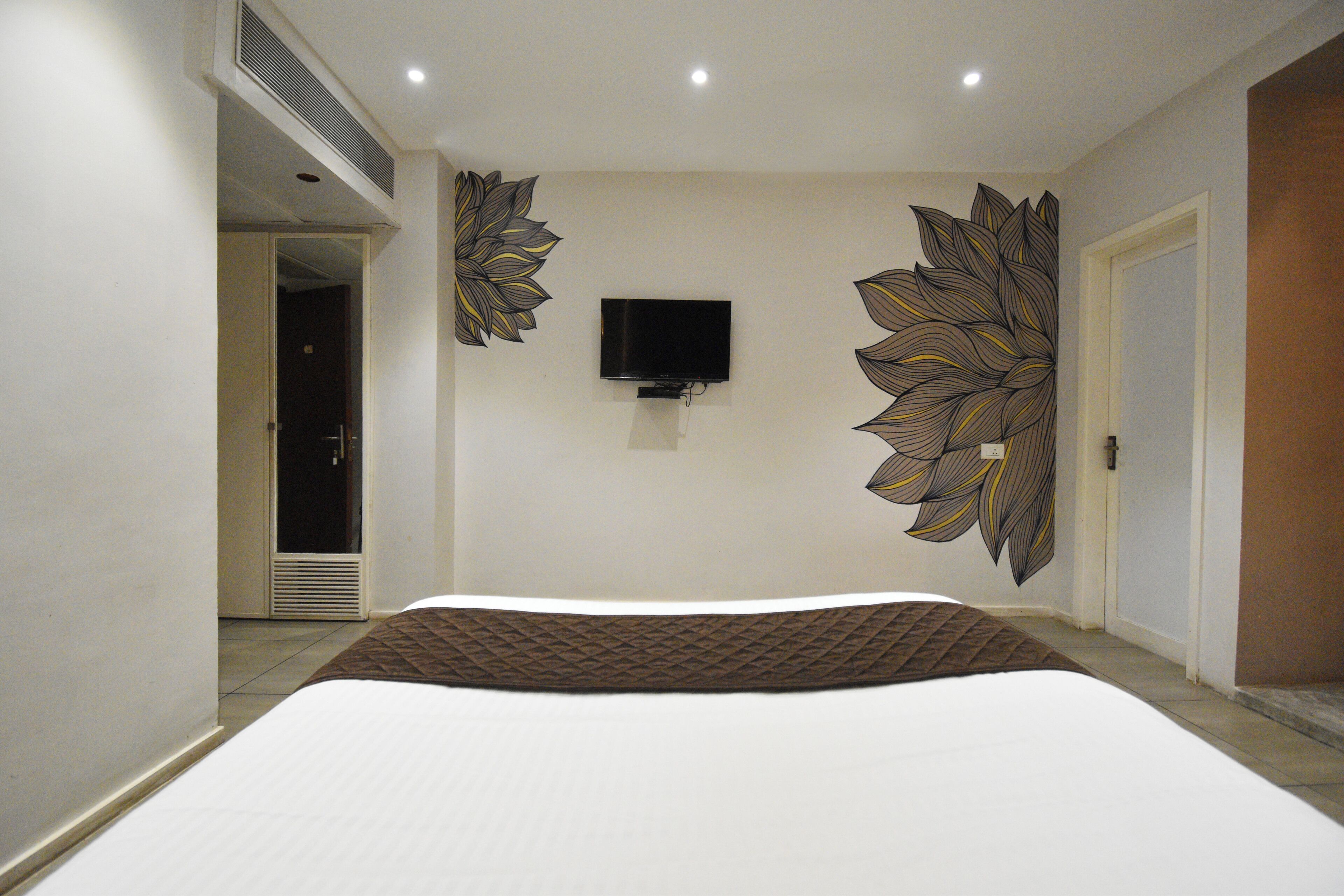 A bedroom with a large bed, a flat-screen TV mounted on the wall, and a decorative leaf pattern on the walls.