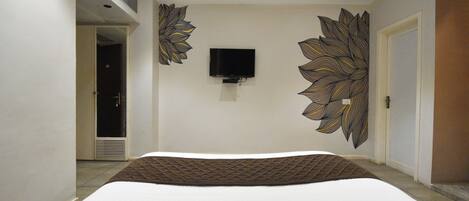 A bedroom with a large bed, a flat-screen TV mounted on the wall, and a decorative leaf pattern on the walls.