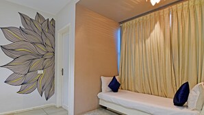 Quarto com sofá branco, cortinas bege e uma grande obra de arte na parede.