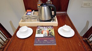 Uma mesa de madeira com uma bandeja contendo uma chaleira, duas garrafas de água, um estojo de lenços e uma revista. Dois copos e pires brancos estão colocados de cada lado da revista.