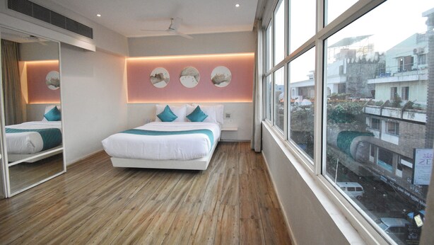 Quarto moderno com uma cama grande, um espelho e vista da cidade através de grandes janelas.