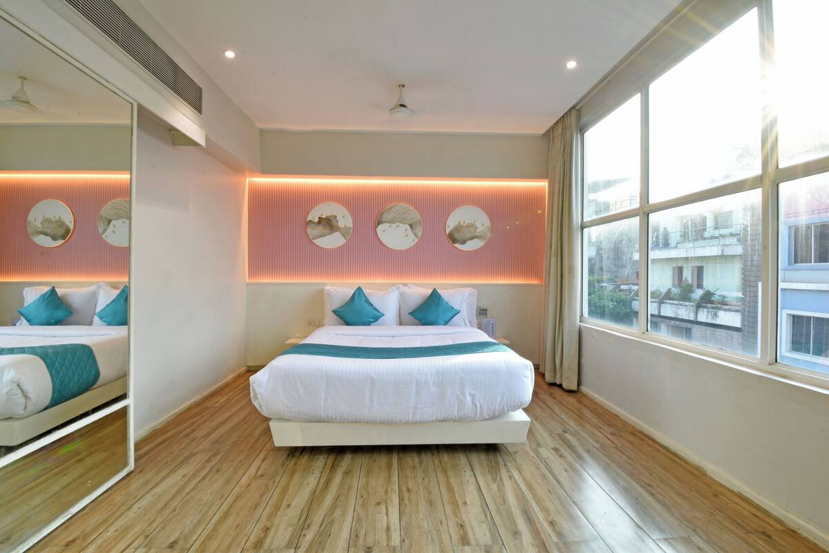 Un dormitorio moderno con una cama grande, un espejo y vistas a la ciudad a través de amplios ventanales.