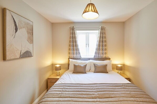 A neatly arranged bedroom with a large bed, two bedside tables, a hanging light fixture, and a window with curtains. - Host & Stay | Sunny Dale Cottage (Pickering)