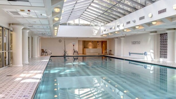 Une vaste piscine intérieure dotée d’un toit en verre, entourée de murs et de colonnes blancs.