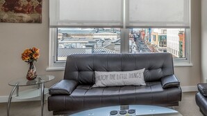 Un salon moderne avec un canapé en cuir, une table basse en verre et une vue sur le paysage urbain grâce à de grandes fenêtres.