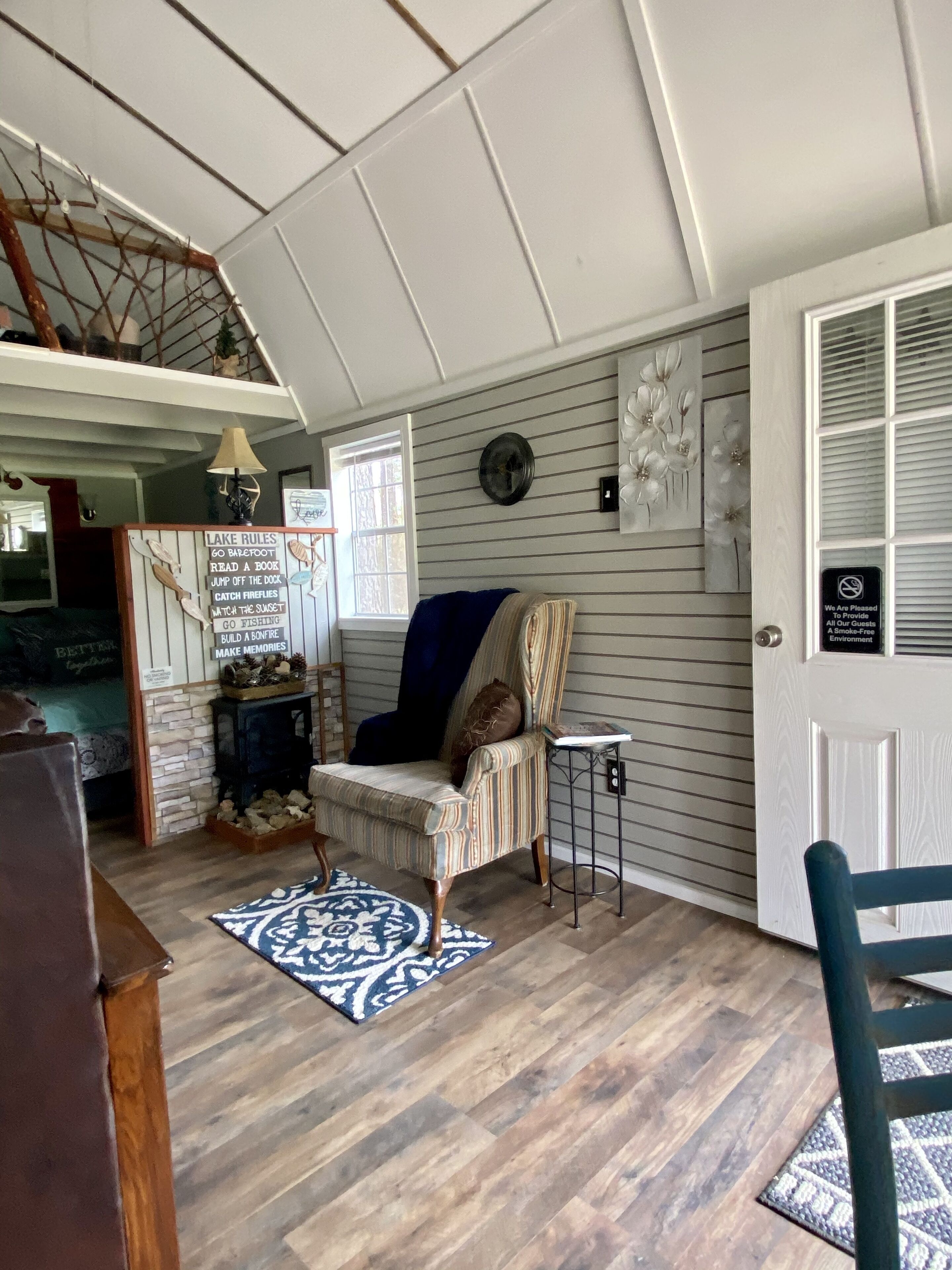 A cozy room with a striped armchair, a blue throw blanket, a patterned rug, a wooden floor, and a wall-mounted clock.