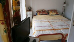 A room with a bed, a desk with a computer, a television, a lamp, and a wall-mounted picture.