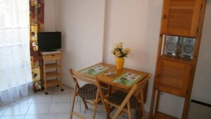 A small room with a wooden desk, two chairs, a TV, a vase with flowers, and a speaker system.