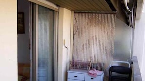 A small balcony with a yellow table, a sliding glass door, a white cabinet, and a chair.