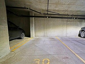 A parking garage with concrete walls, yellow lines marking parking spaces, and a car parked in one of the spaces.